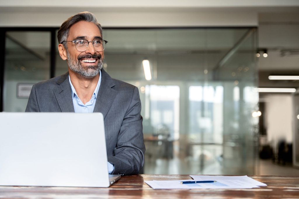 Portrait of mature business man trading using laptop computer, typing, working in modern office.