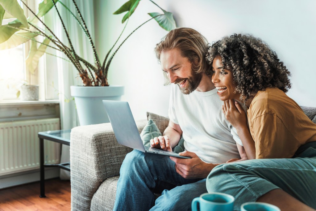 Couple on a couch looking at a laptop smiling